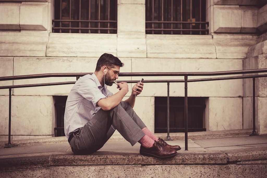 Man with earphones sitting and typing on a phone